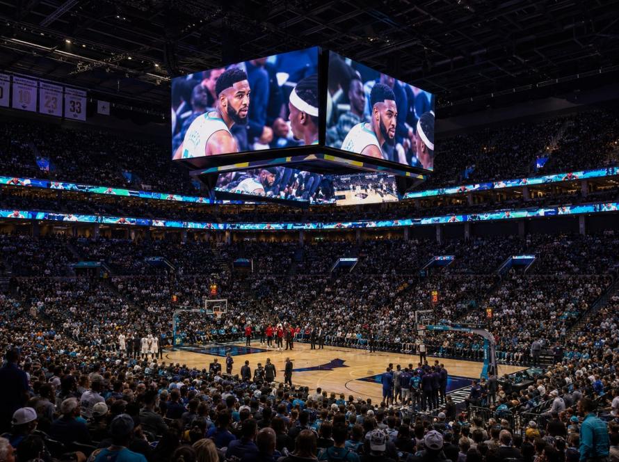 Basketball arena with LED jumbotron and ribbon boards showing live game replay footage above the court